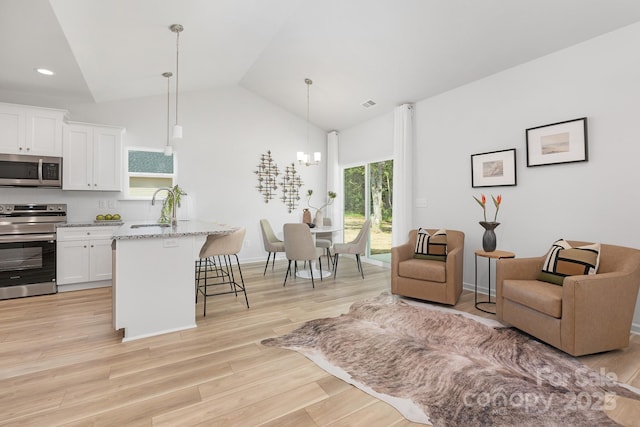 4478 Pebblebrook Cir SW, Concord, NC 28027 - kitchen featuring stainless steel appliances, a kitchen breakfast bar, white cabinets, vaulted ceiling, and light wood-type flooring
