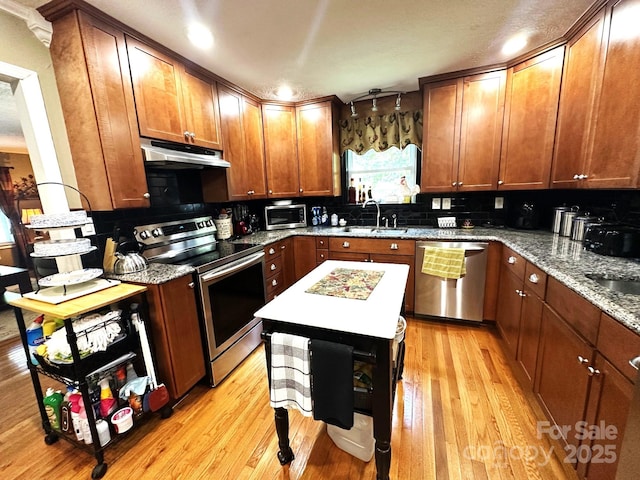 25 Norman Rd, Fletcher, NC 28732 - kitchen with stainless steel appliances, under cabinet range hood, light wood-style floors, light stone countertops, and brown cabinets