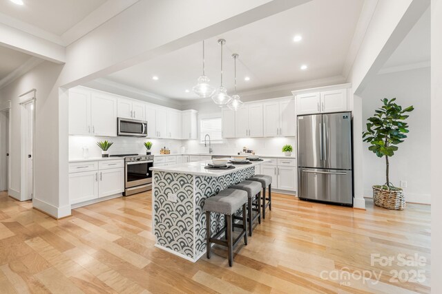 5305 Tarrywood Ln, Charlotte, NC 28205 - kitchen featuring appliances with stainless steel finishes, crown molding, white cabinetry, light wood finished floors, and a kitchen island