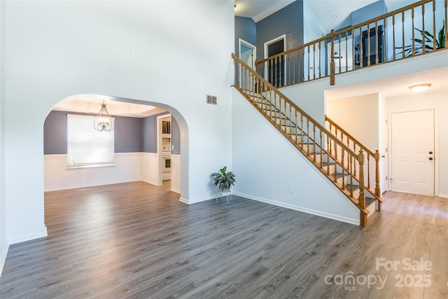 8909 Raven Park Dr, Charlotte, NC 28216 - unfurnished living room featuring wood finished floors, stairway, a wainscoted wall, a chandelier, and arched walkways