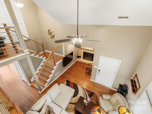 9237 N Vicksburg Park Ct, Charlotte, NC 28210 - living room featuring wood finished floors, a ceiling fan, a glass covered fireplace, stairs, and a high ceiling