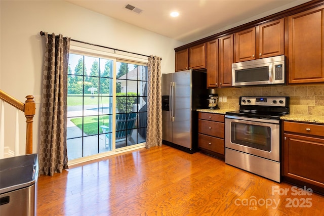 141 Leyton Loop Unit B, Mooresville, NC 28117 - kitchen with appliances with stainless steel finishes, decorative backsplash, light stone countertops, light wood-type flooring, and brown cabinetry