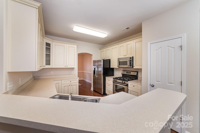 9836 Coatbridge Dr NW, Charlotte, NC 28269 - kitchen featuring stainless steel appliances, cream cabinetry, light countertops, glass insert cabinets, and arched walkways