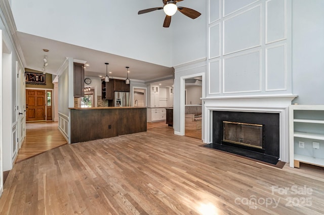 6225 Ash Cove Ln, Charlotte, NC 28269 - unfurnished living room with crown molding, ceiling fan, light wood finished floors, a high ceiling, and a fireplace with flush hearth