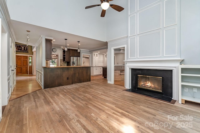 6225 Ash Cove Ln, Charlotte, NC 28269 - unfurnished living room with crown molding, light wood-type flooring, ceiling fan, a fireplace with flush hearth, and a high ceiling
