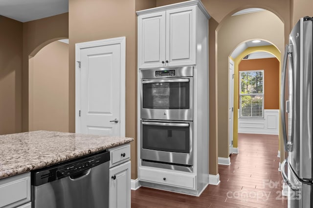 113 Chaska Loop, Troutman, NC 28166 - kitchen with appliances with stainless steel finishes, white cabinets, dark wood-type flooring, arched walkways, and light stone counters