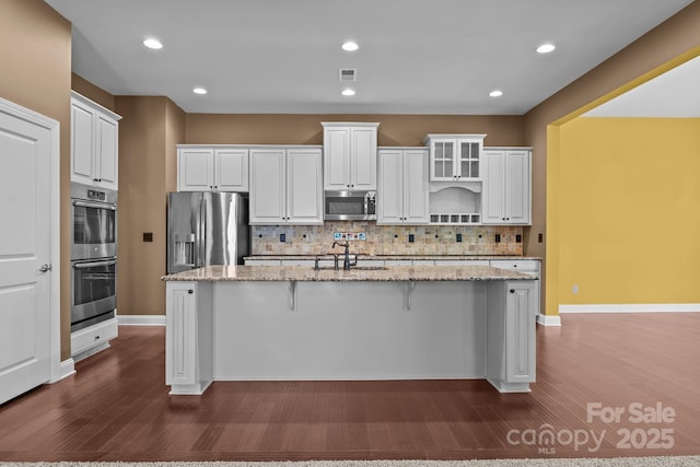 113 Chaska Loop, Troutman, NC 28166 - kitchen with appliances with stainless steel finishes, a center island with sink, dark wood-style floors, tasteful backsplash, and white cabinets