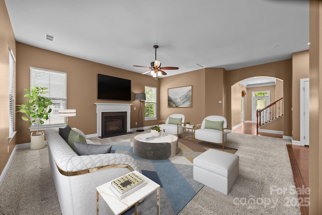 113 Chaska Loop, Troutman, NC 28166 - living room with arched walkways, a glass covered fireplace, ceiling fan, carpet, and stairway