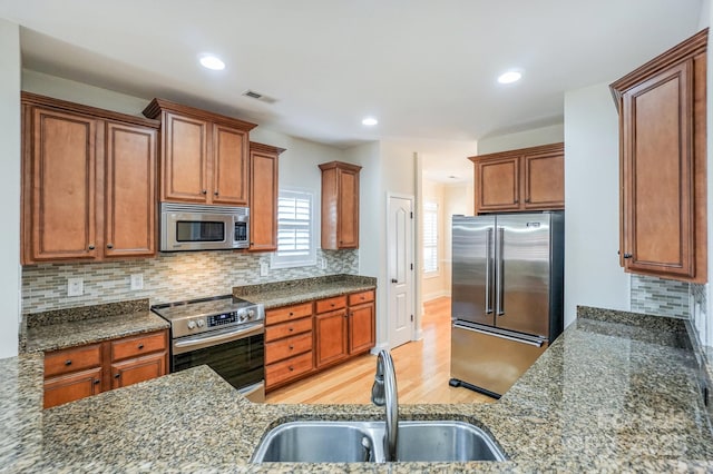 19421 Beaufain St, Cornelius, NC 28031 - kitchen featuring appliances with stainless steel finishes, light wood-style flooring, dark stone counters, tasteful backsplash, and recessed lighting