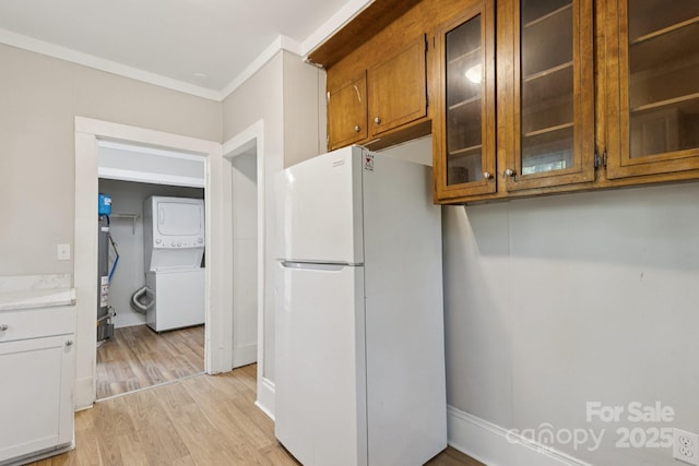 709 E Front St, Statesville, NC 28677 - kitchen with freestanding refrigerator, estacked washer and dryer, brown cabinets, light wood-style floors, and ornamental molding