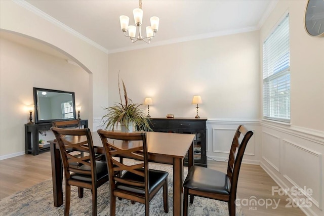 2309 Abundance Ln, Waxhaw, NC 28173 - dining space featuring light wood-type flooring, a chandelier, arched walkways, crown molding, and a wainscoted wall