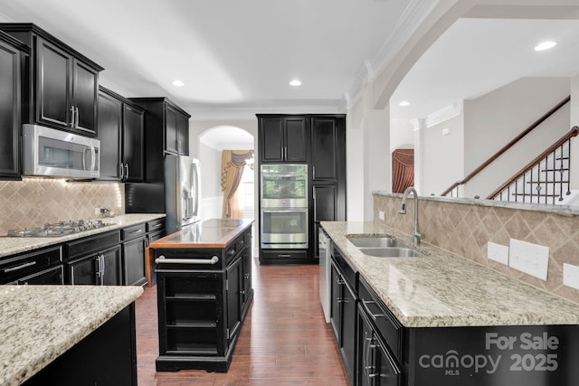 12515 Hashanli Pl, Matthews, NC 28105 - kitchen featuring arched walkways, dark cabinetry, stainless steel appliances, an island with sink, and crown molding