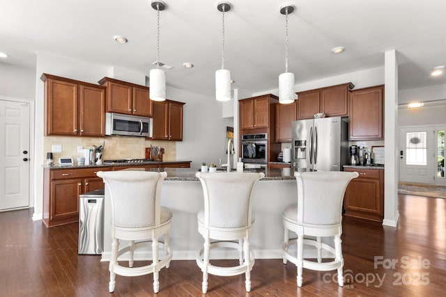 2005 Brightflower Ln, York, SC 29745 - kitchen with appliances with stainless steel finishes, a center island with sink, tasteful backsplash, brown cabinets, and dark wood finished floors