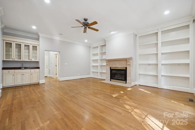 18802 Pentwater Ct, Cornelius, NC 28031 - unfurnished living room featuring built in shelves, a ceiling fan, a glass covered fireplace, crown molding, and light wood-type flooring