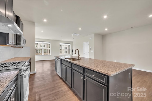 2004 Dornoch Rd, Tega Cay, SC 29708 - kitchen with appliances with stainless steel finishes, wall chimney range hood, a center island with sink, wood finished floors, and recessed lighting
