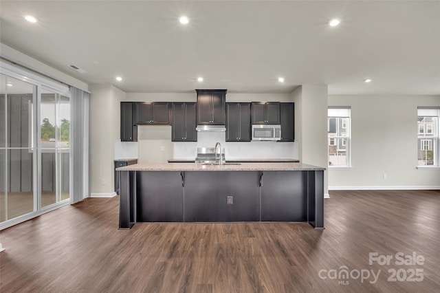 2004 Dornoch Rd, Tega Cay, SC 29708 - kitchen with stainless steel microwave, dark wood-type flooring, a center island with sink, recessed lighting, and light stone counters