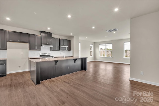 2004 Dornoch Rd, Tega Cay, SC 29708 - kitchen with appliances with stainless steel finishes, an island with sink, dark wood-style flooring, recessed lighting, and a kitchen bar