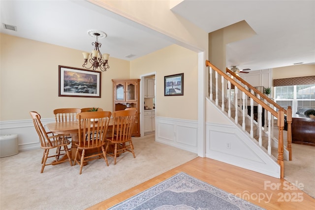 5630 Cambridge Bay Dr, Charlotte, NC 28269 - dining area featuring stairs, a chandelier, light wood-type flooring, wainscoting, and a decorative wall