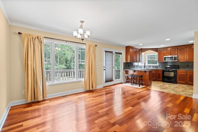 1566 Mayfair Dr, Conover, NC 28613 - kitchen with black electric range oven, stainless steel microwave, a chandelier, light wood finished floors, and a breakfast bar area