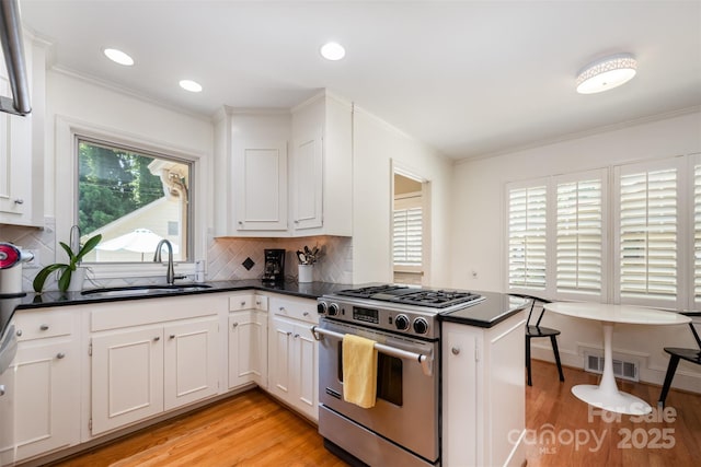 7119 Folger Dr, Charlotte, NC 28270 - kitchen with stainless steel gas range oven, dark countertops, light wood-style flooring, a peninsula, and crown molding