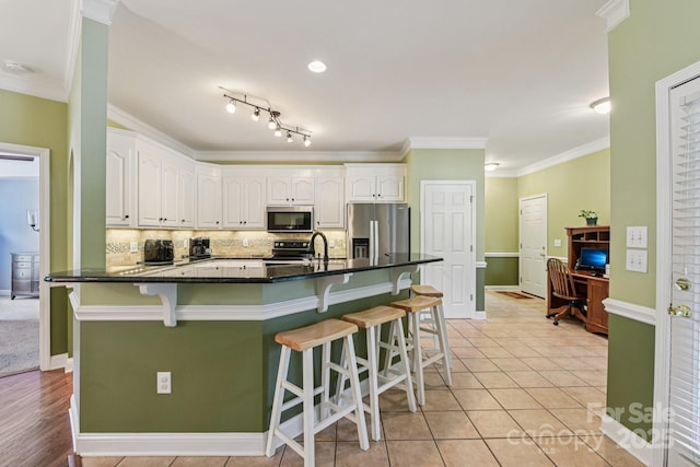 3865 Willow Grove Ln, Concord, NC 28025 - kitchen featuring appliances with stainless steel finishes, white cabinetry, a kitchen bar, crown molding, and a desk