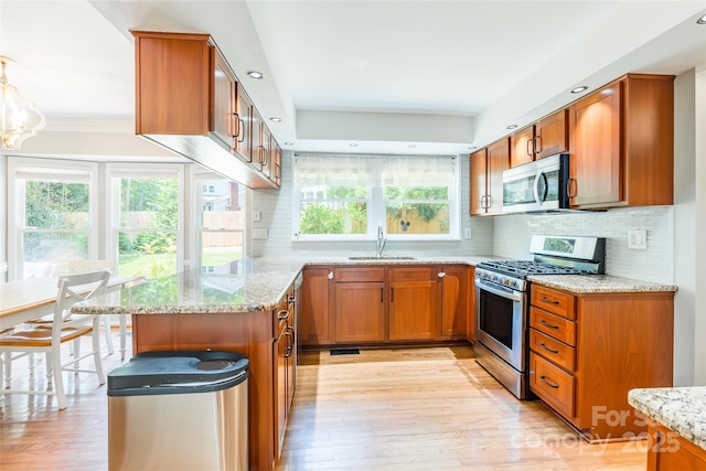 1220 Merribrook Dr, Matthews, NC 28105 - kitchen featuring appliances with stainless steel finishes, brown cabinets, a peninsula, light stone countertops, and healthy amount of natural light
