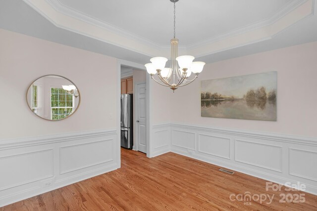 8606 Gresham Dr, Waxhaw, NC 28173 - unfurnished room with a chandelier, a raised ceiling, light wood-type flooring, ornamental molding, and a wainscoted wall