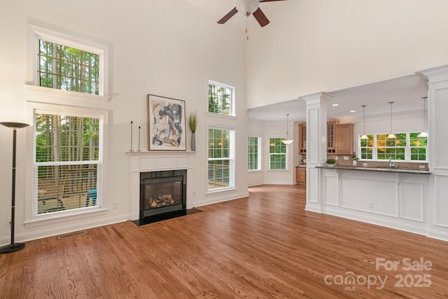 8606 Gresham Dr, Waxhaw, NC 28173 - unfurnished living room featuring a ceiling fan, light wood-style flooring, a high ceiling, a fireplace with flush hearth, and healthy amount of natural light