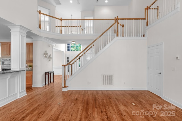 8606 Gresham Dr, Waxhaw, NC 28173 - unfurnished living room featuring a towering ceiling, stairs, light wood-style floors, and decorative columns