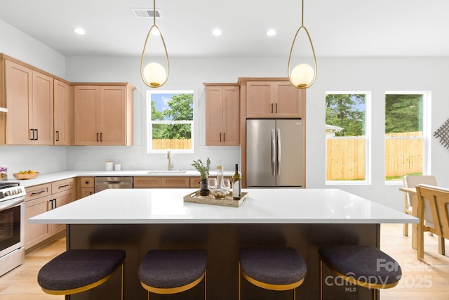 2417 Pruitt St, Charlotte, NC 28208 - kitchen with appliances with stainless steel finishes, a breakfast bar, light countertops, light brown cabinets, and recessed lighting