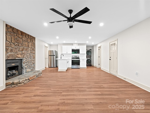 1065 Oak Ridge Ln, Mars Hill, NC 28754 - unfurnished living room featuring stacked washer / drying machine, ceiling fan, recessed lighting, a stone fireplace, and light wood-style floors