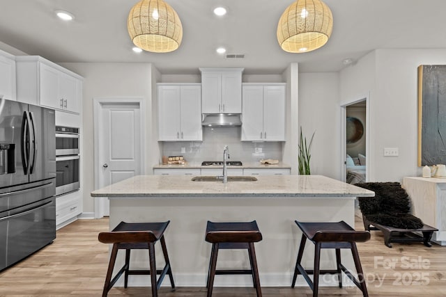 9021 Myrna Dr, Gastonia, NC 28056 - kitchen featuring stainless steel appliances, under cabinet range hood, tasteful backsplash, white cabinets, and a kitchen bar