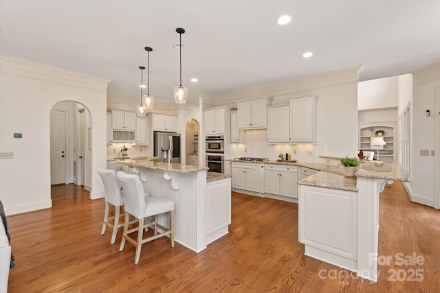 1505 Hawkstone Dr, Waxhaw, NC 28173 - kitchen featuring appliances with stainless steel finishes, a kitchen bar, arched walkways, crown molding, and a peninsula