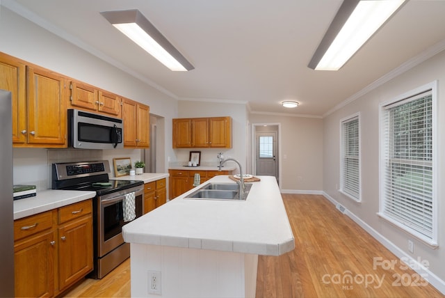 1408 Wildwood Dr, Kannapolis, NC 28081 - kitchen featuring stainless steel appliances, ornamental molding, light countertops, light wood-style flooring, and a kitchen island with sink