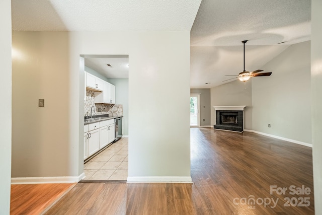 8027 Sherington Way, Charlotte, NC 28227 - unfurnished living room with a ceiling fan, light wood-type flooring, a fireplace with raised hearth, vaulted ceiling, and a textured ceiling