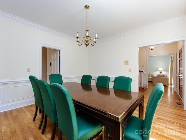 9413 Tillot Dr, Matthews, NC 28105 - dining room with crown molding, a chandelier, light wood finished floors, a wainscoted wall, and a decorative wall
