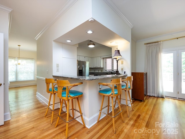 9413 Tillot Dr, Matthews, NC 28105 - kitchen with light wood-style floors, ornamental molding, a peninsula, white cabinets, and a breakfast bar area