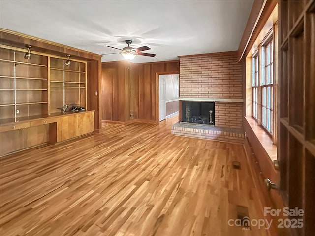 208 N Gaston St, Kings Mountain, NC 28086 - unfurnished living room with a brick fireplace, light wood-type flooring, a ceiling fan, and wooden walls