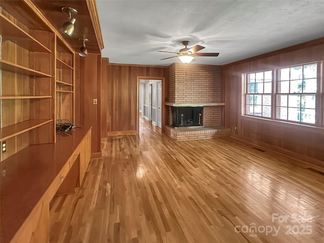 208 N Gaston St, Kings Mountain, NC 28086 - unfurnished living room with ceiling fan, a brick fireplace, wooden walls, light wood-style floors, and crown molding