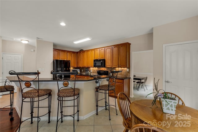 1993 W Foxwood Ct, Indian Land, SC 29707 - kitchen with black appliances, a kitchen bar, dark countertops, brown cabinetry, and backsplash