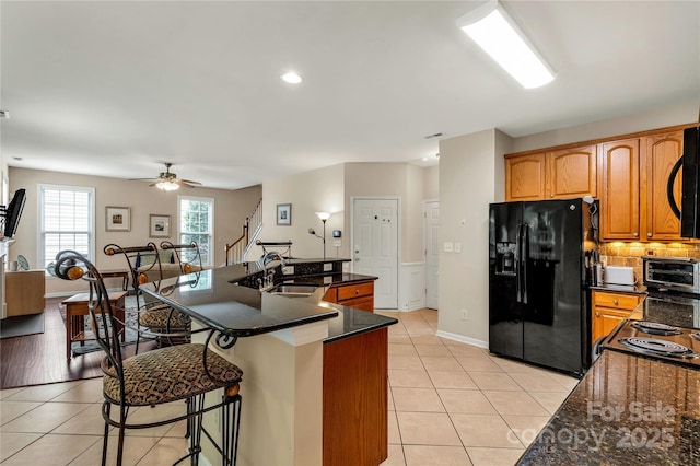 1993 W Foxwood Ct, Indian Land, SC 29707 - kitchen featuring black refrigerator with ice dispenser, light tile patterned floors, a breakfast bar, ceiling fan, and decorative backsplash