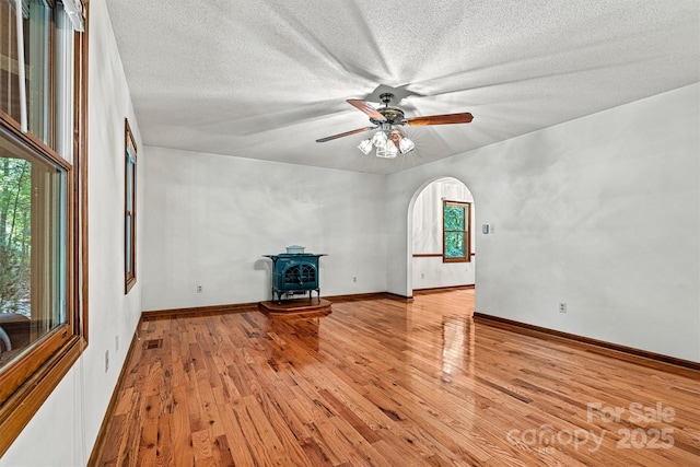 1408 Kensington Cir, Newton, NC 28658 - unfurnished living room featuring a ceiling fan, a wood stove, light wood-type flooring, a textured ceiling, and arched walkways