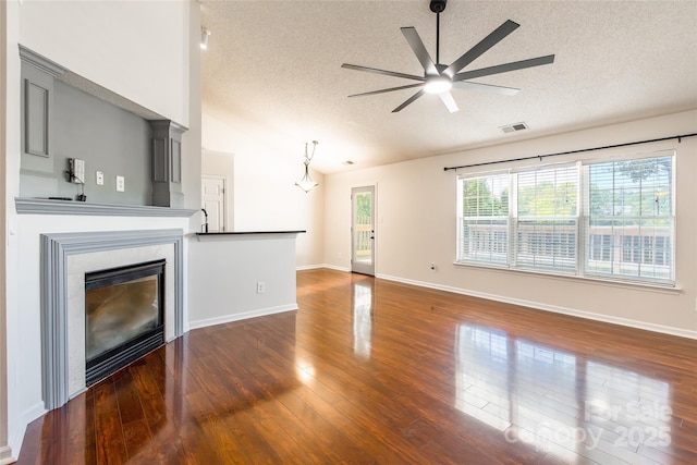 14924 Jerpoint Abby Dr, Charlotte, NC 28273 - unfurnished living room featuring a textured ceiling, vaulted ceiling, a ceiling fan, dark wood-style flooring, and a glass covered fireplace