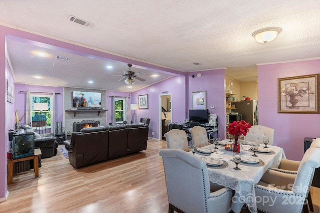 115 Red Fox Ct, Mount Holly, NC 28120 - dining room featuring light wood-style flooring, ceiling fan, a textured ceiling, ornamental molding, and a warm lit fireplace