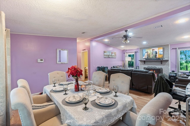 115 Red Fox Ct, Mount Holly, NC 28120 - dining area featuring a textured ceiling, light wood-type flooring, ornamental molding, a ceiling fan, and a lit fireplace
