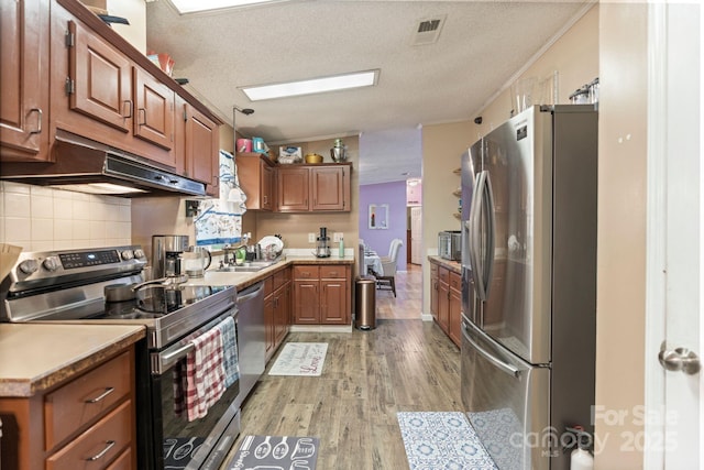 115 Red Fox Ct, Mount Holly, NC 28120 - kitchen featuring stainless steel appliances, light wood-style flooring, brown cabinets, under cabinet range hood, and decorative backsplash