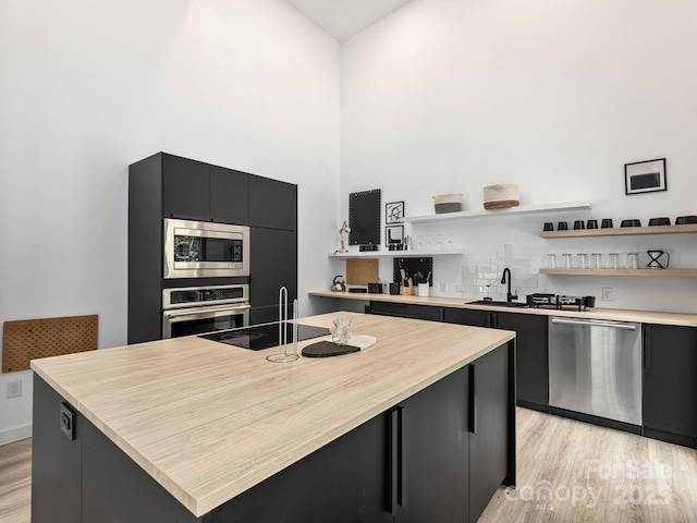 1761 Williamson Creek Rd, Pisgah Forest, NC 28768 - kitchen featuring dark cabinetry, open shelves, stainless steel appliances, light wood-style flooring, and a kitchen island