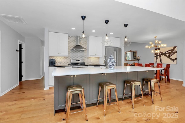 4906 Crooked Oak Ln, Charlotte, NC 28226 - kitchen featuring wall chimney exhaust hood, appliances with stainless steel finishes, white cabinetry, light wood-type flooring, and a large island with sink