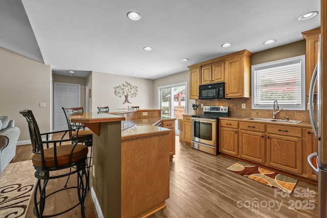 1974 Redwood Dr, Oakboro, NC 28129 - kitchen featuring stainless steel electric range, black microwave, a kitchen breakfast bar, wood finished floors, and decorative backsplash