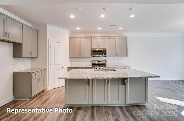 3238 Bozeman Ct Unit 07, Denver, NC 28164 - kitchen featuring appliances with stainless steel finishes, gray cabinetry, crown molding, light stone counters, and a kitchen island with sink